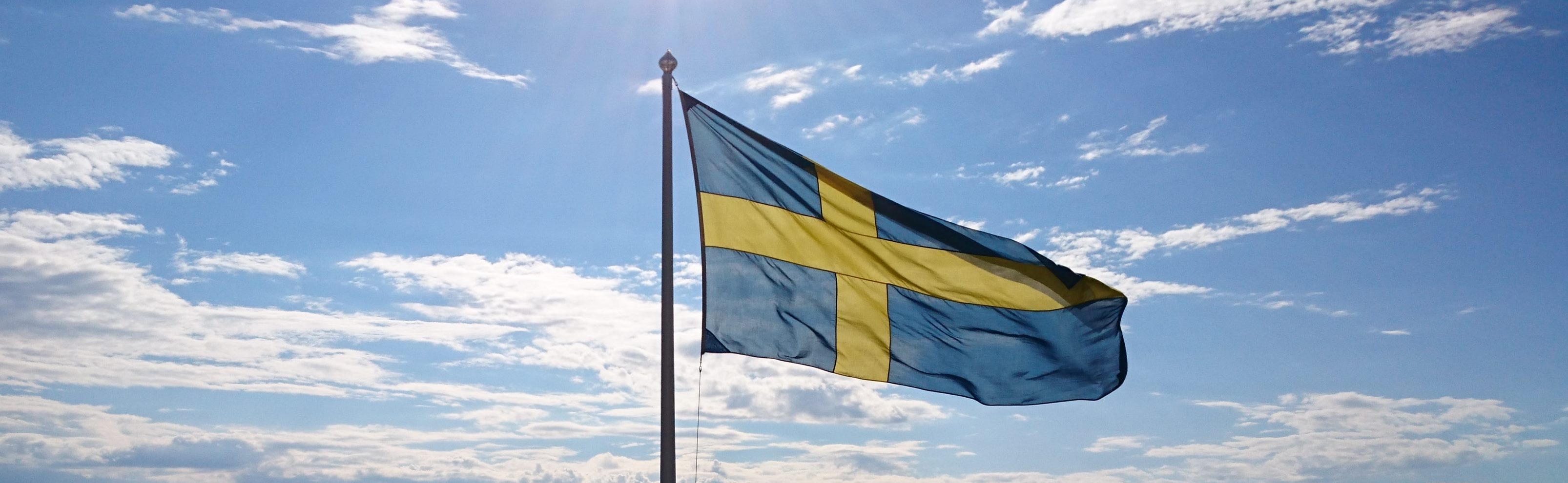 En svensk flagga mot en blå himmel med lite moln.