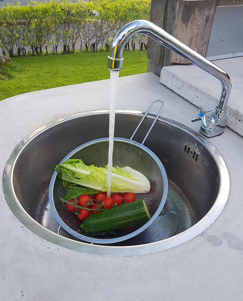 Kran spolar vatten på grönsaker som ligger i utekökets slask.
