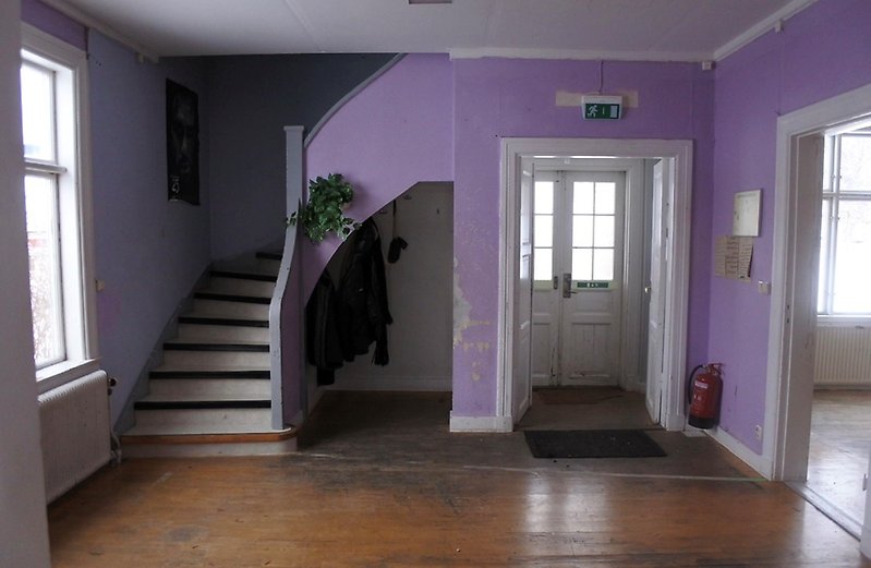 En hall med en trappa till övervåningen. Väggarna är lila och färgen har släppt på en del ställen.